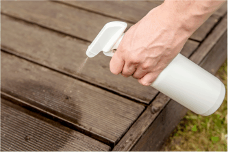 spraying a homemade ant spray outside on the deck