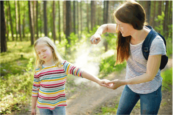 a mom spraying bug spray onto her daughter